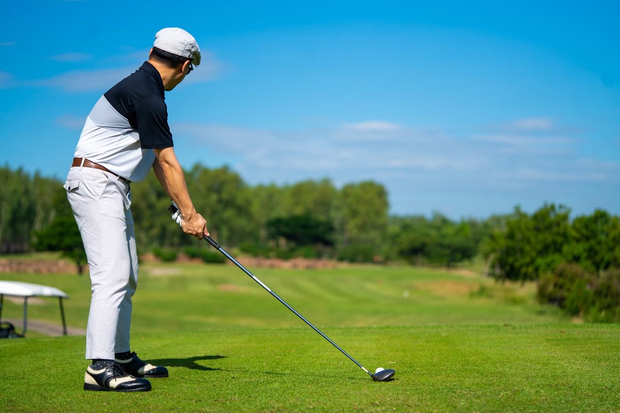 A golfer holding golf club hitting golf ball on the green at golf course in sunny day
