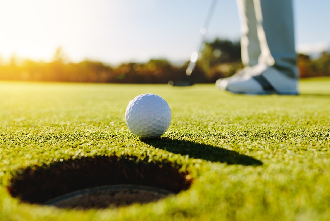 A close up of a putting ball almost in with the golfer’s feet and club in the background