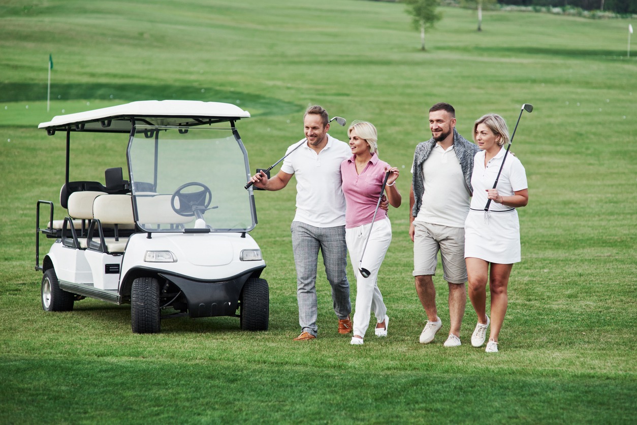 The group of family friends walking around on the field after the golf game with vehicle behind