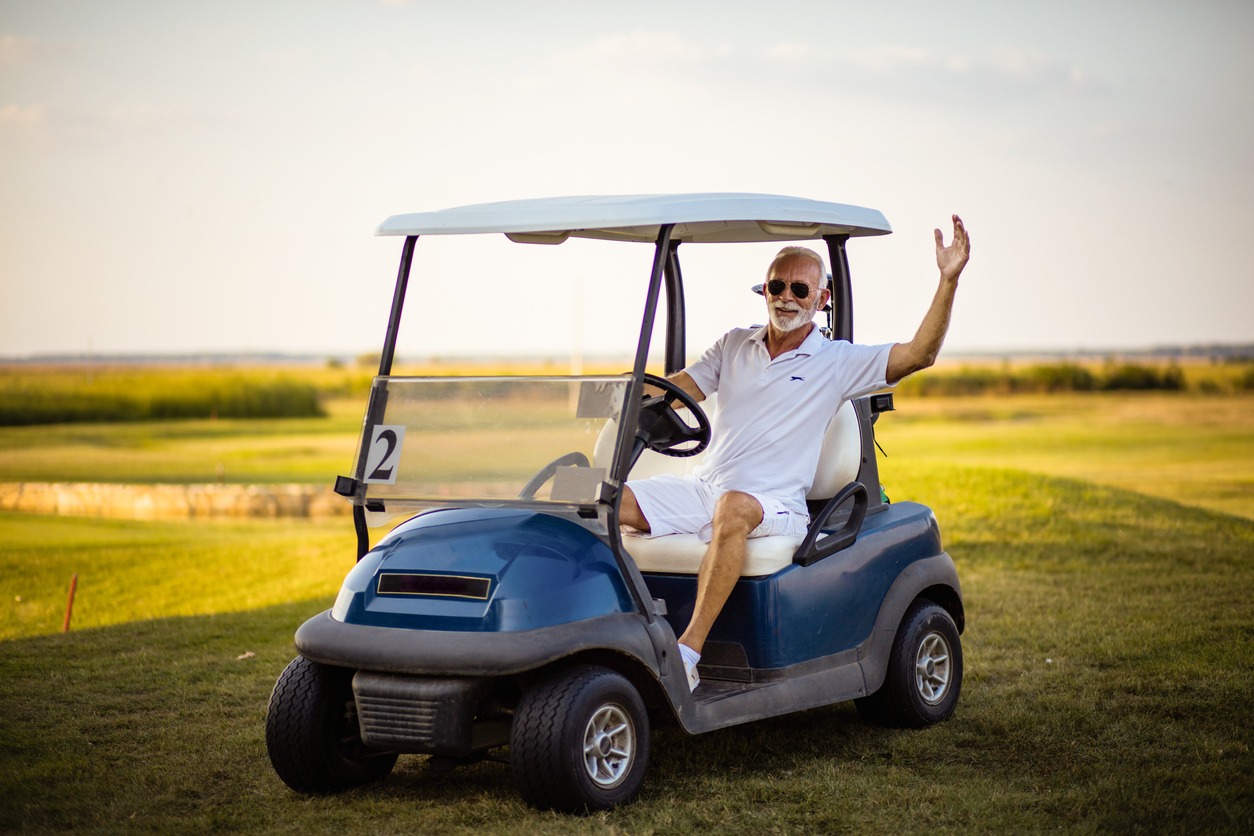 an old male golfer happily driving a golf cart on the course