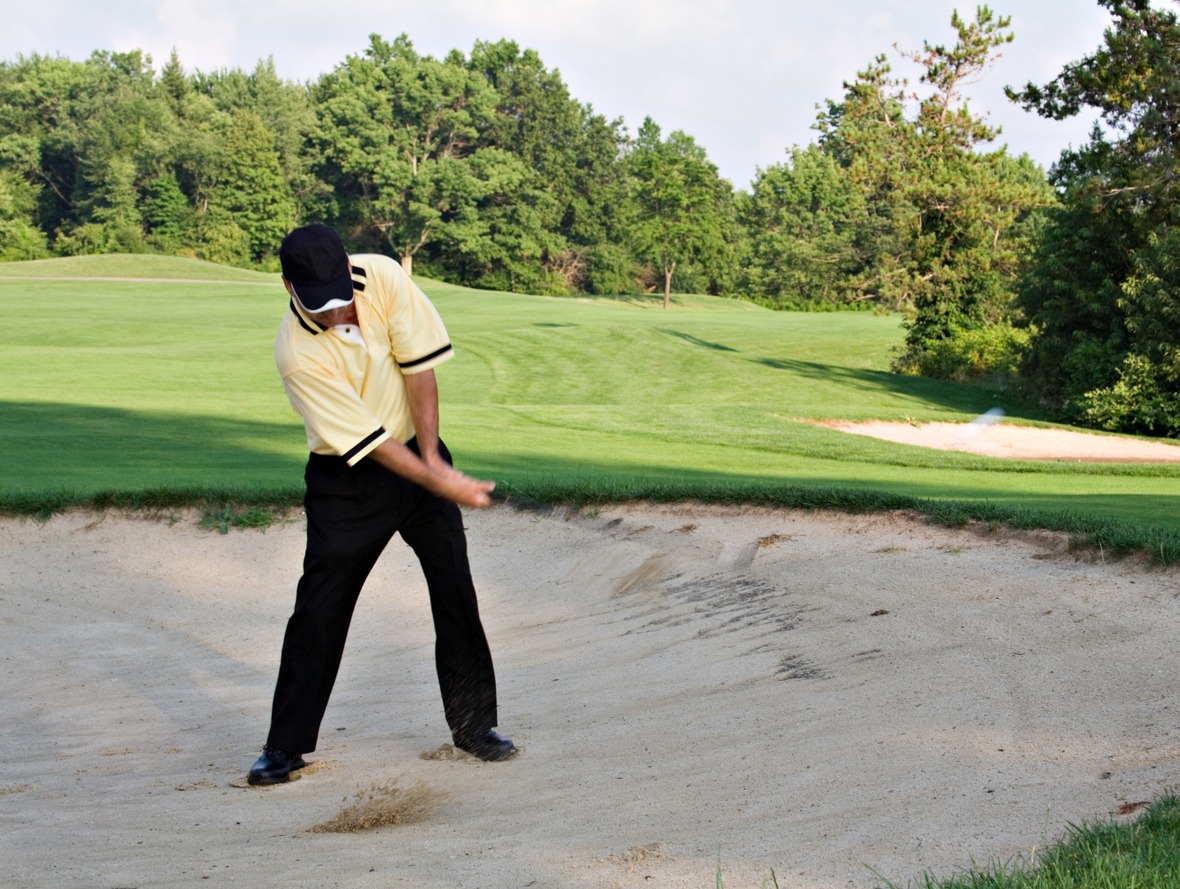 Man hits ball out of sand trap - motion blur on club and ball in flight