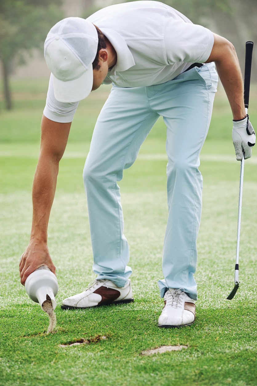 Young man repairing the divot during his game of golf