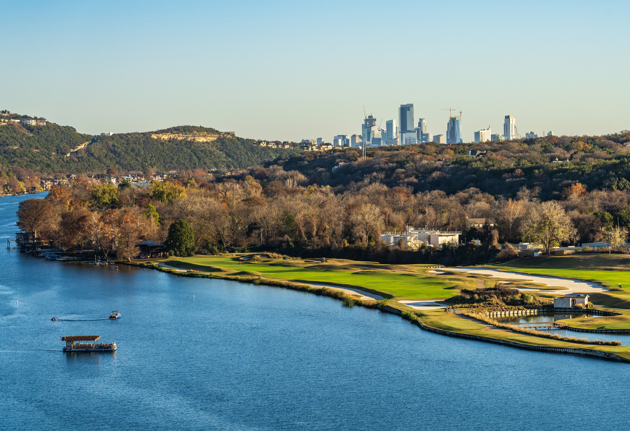 a golf course lining the Colorado river with downtown Austin Texas in distance from Pennybacker bridge overlook