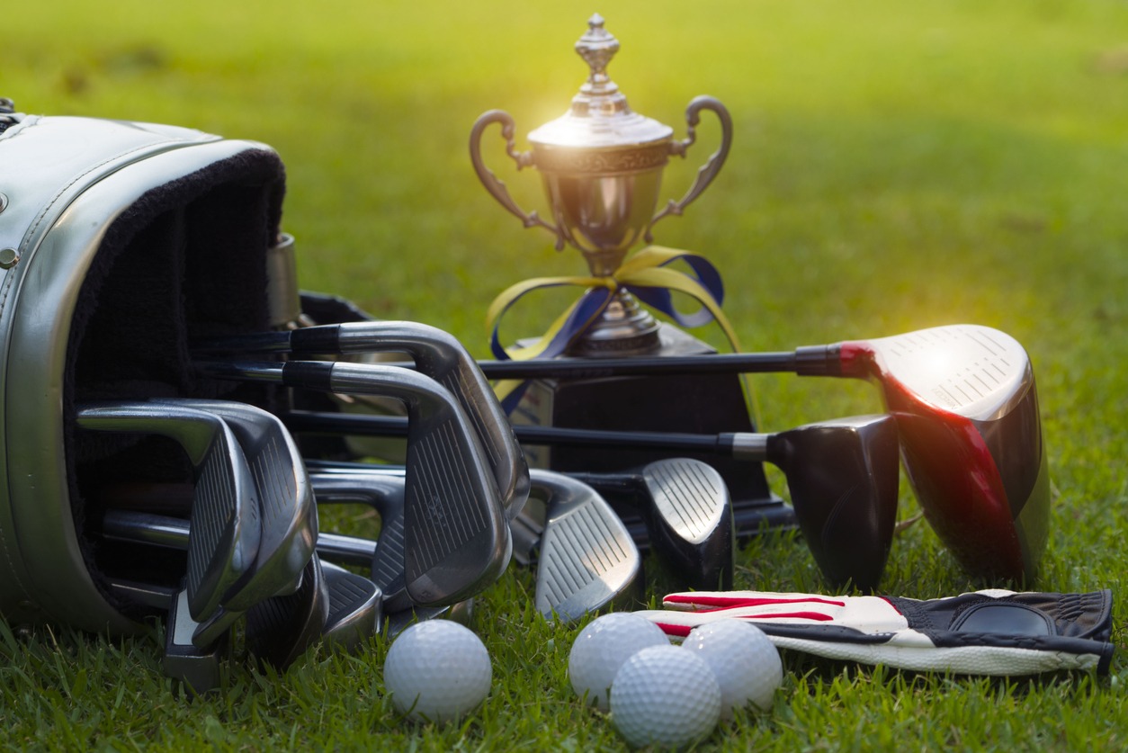 A close up of various clubs in a golf bag an a trophy on the background
