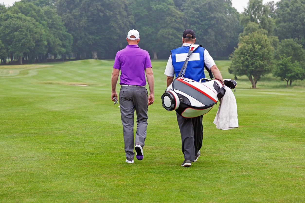 A golfer and caddie walking away in a golf course