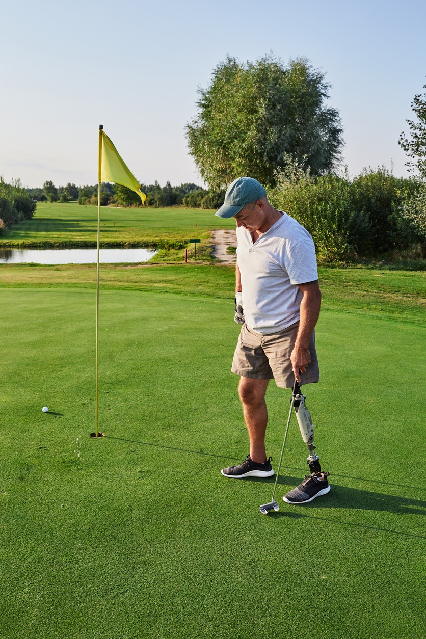 Adult man with a artificial leg playing golf outdoor at green golf course