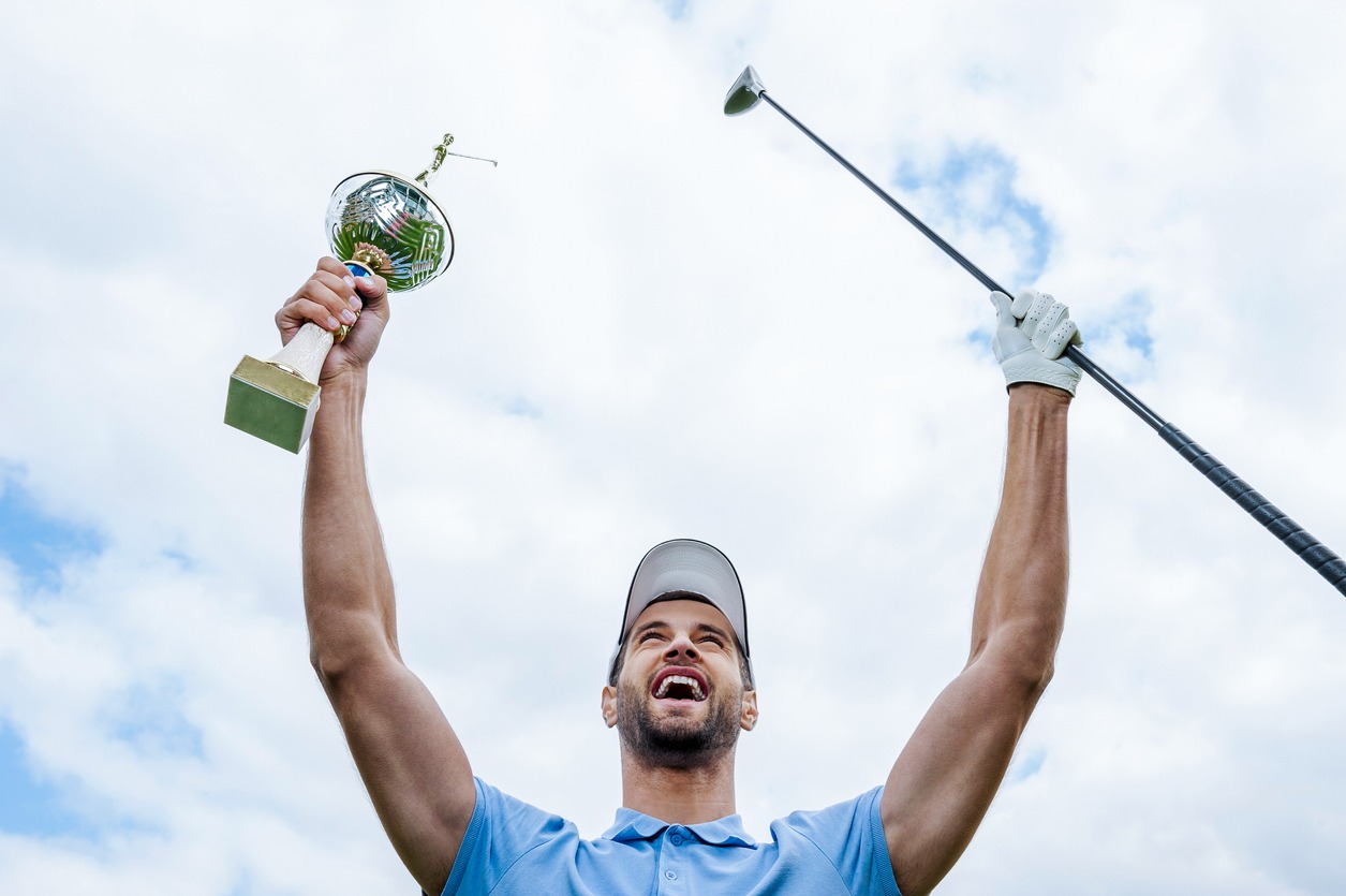 Golfer celebrating by lifting trophy and golfclub in the air