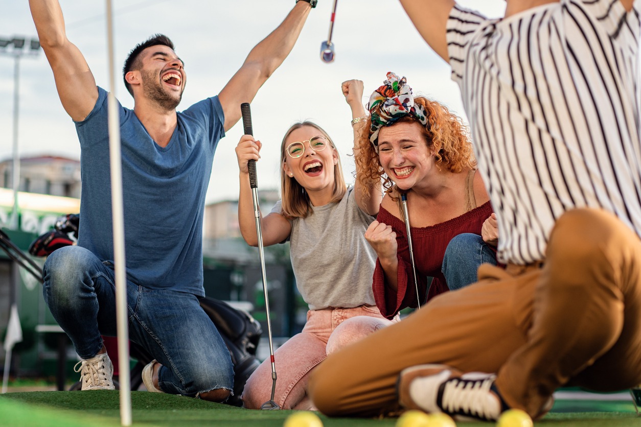 Group of smiling friends enjoying together playing mini golf