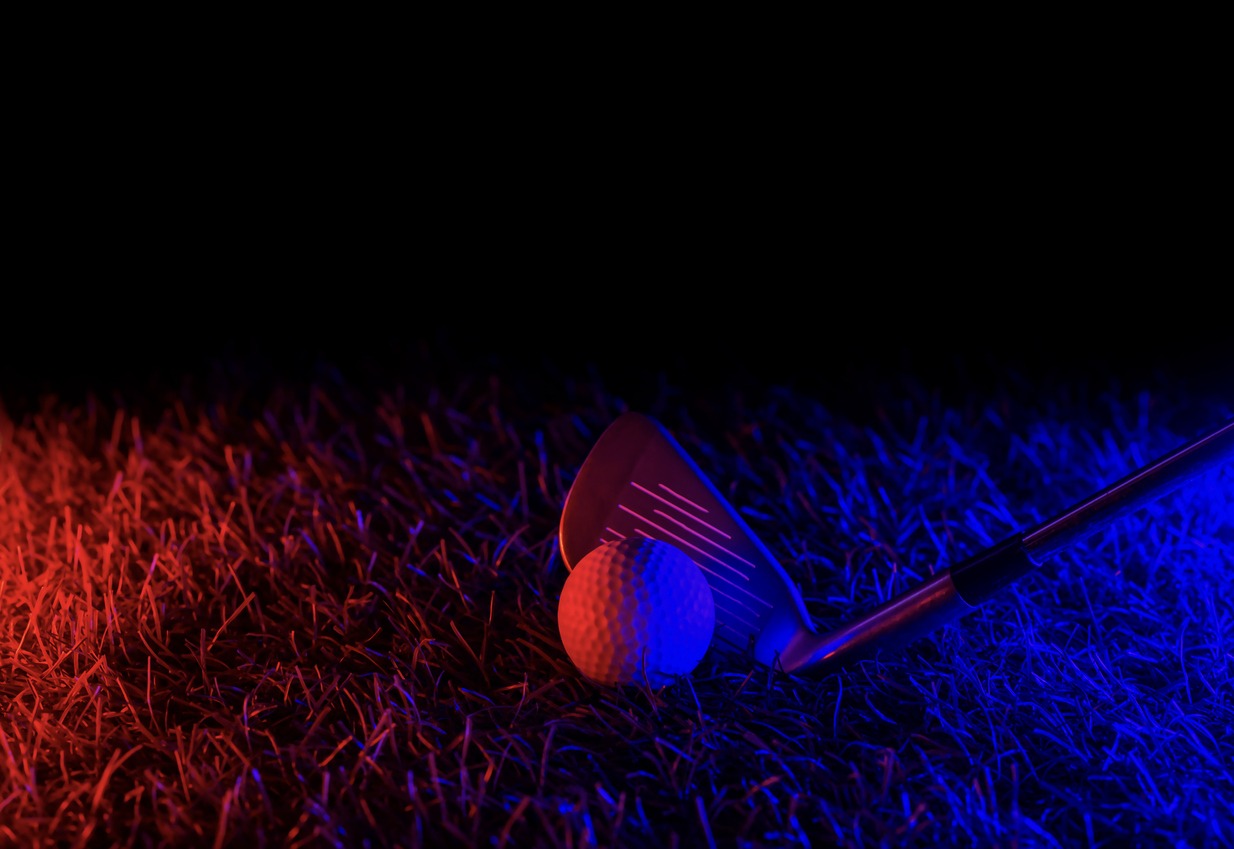 golf stick and white ball on the grass under the glow of red-and-blue neon lights